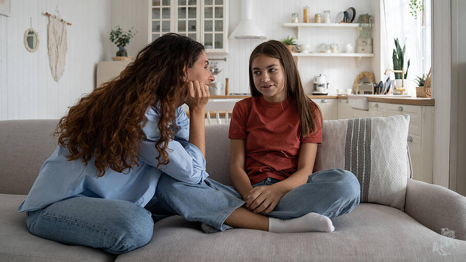 Glückliche, gutmütige Mutter sitzt zu Hause auf der Couch mit einem Mädchen im Teenageralter und träumt von der Zukunft