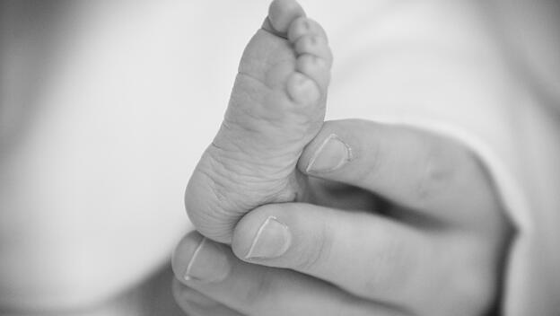 Elternteil hält Fuß seines toten Neugeborenen