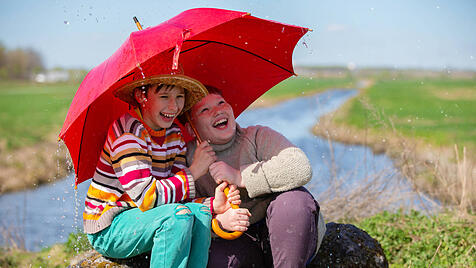 Zwei Freunde lachen unter einem Regenschirm im Regen. Kinder werden im Freien vom Regen überrascht.