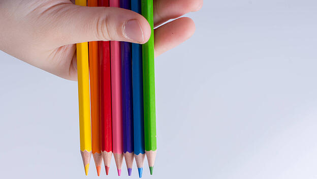 Hand mit Buntstiften in Regenbogenfarben