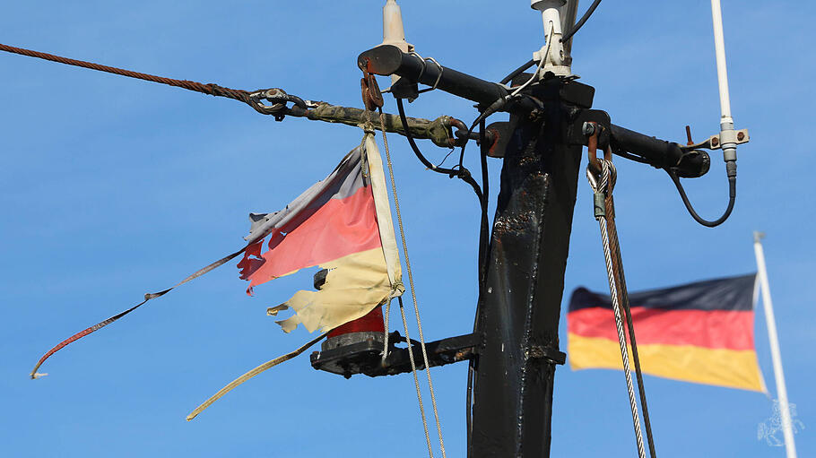 Eine zerrissene Flagge der Bundesrepublik Deutschland an dem Mast eines Fischkutters.