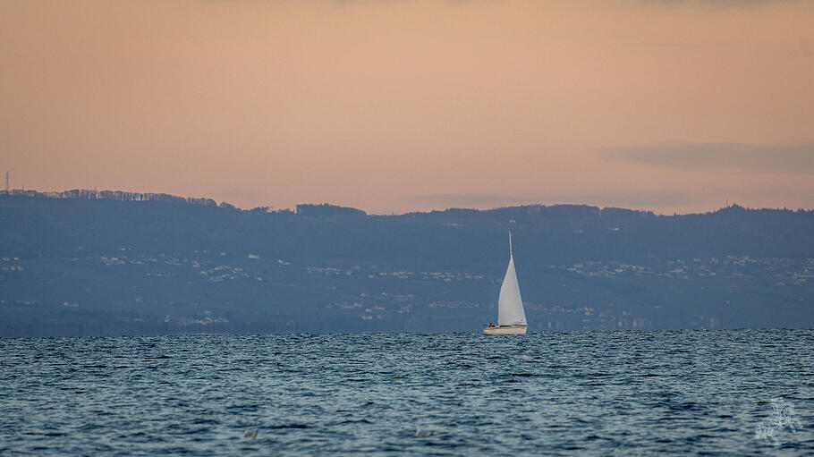 A serene scene of a sailboat gracefully moving across a calm lake in Geneva, set against a backdrop of distant hills dur