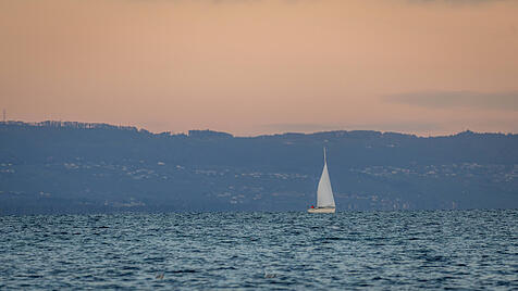 A serene scene of a sailboat gracefully moving across a calm lake in Geneva, set against a backdrop of distant hills dur