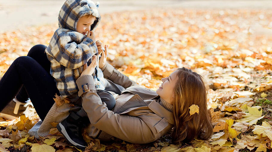 Happy mother playing with son lying on autumn leaves in park model released, Symbolfoto, ONAF00218