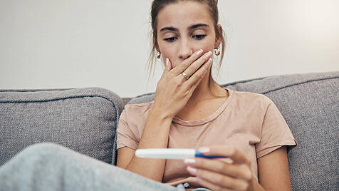 Pregnancy test, surprise and woman on sofa in home, reading bad news and check negative results. Pregnant, stick and sad