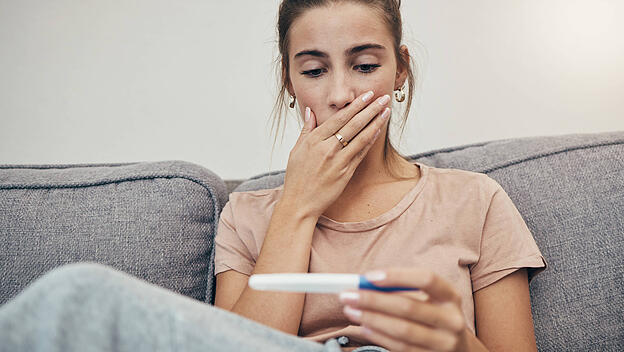 Pregnancy test, surprise and woman on sofa in home, reading bad news and check negative results. Pregnant, stick and sad
