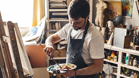 Male painter at art studio indoors with palette mixing colors ready to draw concentrated