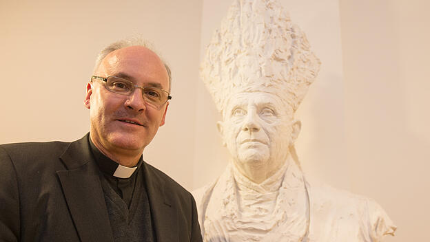 Bischof Rudolf Voderholzer neben einer Büste von Papst Benedikt XVI.