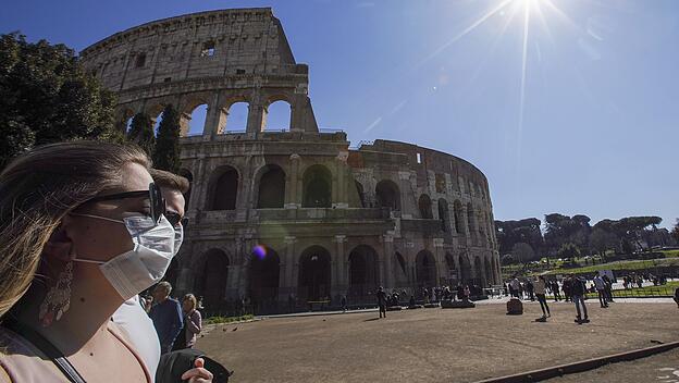 Touristen gehen mit Mundschutz am Kolosseum vorbei.