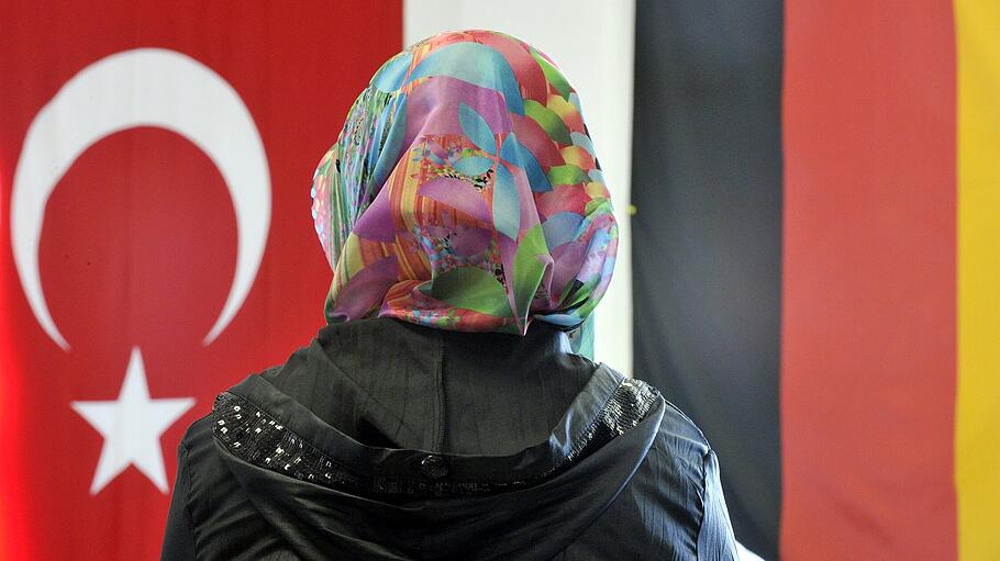 Frau mit Kopftuch vor deutscher und türkischer Flagge