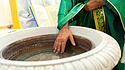 Ein Priester segnet während einer Taufzeremonie das Wasser eines marmornen Taufbeckens