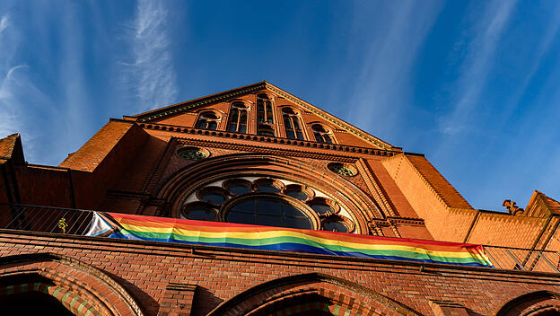 Eine Regenbogen-Fahne hängt an der Fassade der Heilig-Kreuz-Kirche in Berlin