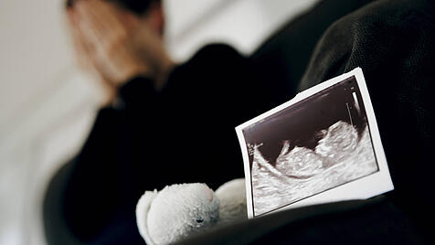 Symbolfoto: Gestellte Aufnahme zum Thema Fehlgeburt. Das Ultraschallbild eines ungeborenen Kindes steht neben einem Kusc