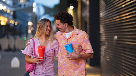 Gen Z couple in pink outfits leaving the cinema with drinks in hand. Gen Z couple in pink outfits leaving the cinema wit
