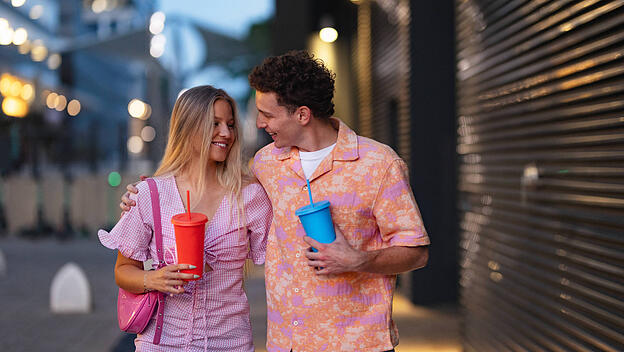 Gen Z couple in pink outfits leaving the cinema with drinks in hand. Gen Z couple in pink outfits leaving the cinema wit