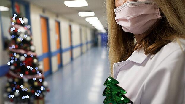 Krankenhauspersonal mit weihnachtlicher Dekoration in der Kitteltasche und mit Mund- und Nasenschutzmaske neben einem ge