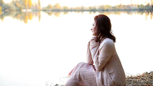 Eine Frau sitzt am Ufer eines Sees