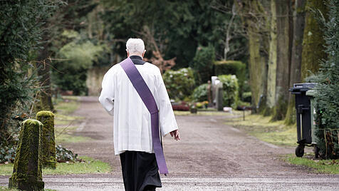 Katholischer Priester geht während einer Beerdigung über einen Friedhofsweg