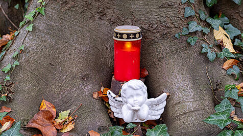 Engelfigur und Grablicht an einem Baum