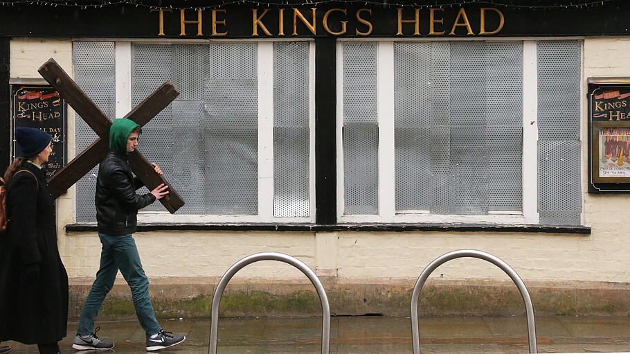Ein Mann trägt ein Holzkreuz durch die Straßen Londons