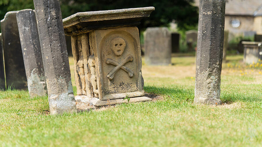 Ein alter Grabstein auf einem englischen Friedhof zeigt Schädel und Knochen als Symbole für den Tod.