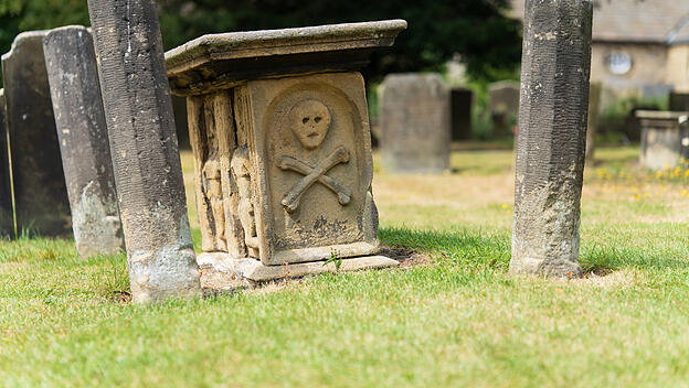 Ein alter Grabstein auf einem englischen Friedhof zeigt Sch&auml;del und Knochen als Symbole f&uuml;r den Tod.
