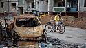 Zwei Jungen schieben Fahrräder vorbei an zerstörte Autos und Wohngebäude in Tschernihiw.