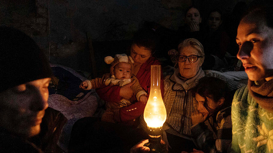 Menschen sitzen um eine Lampe in einem Bunker in Mariupol