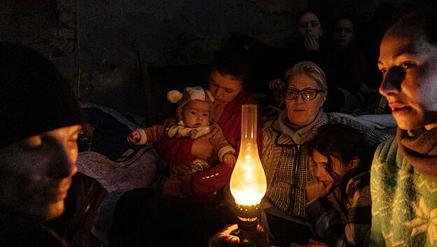 Menschen sitzen um eine Lampe in einem Bunker in Mariupol