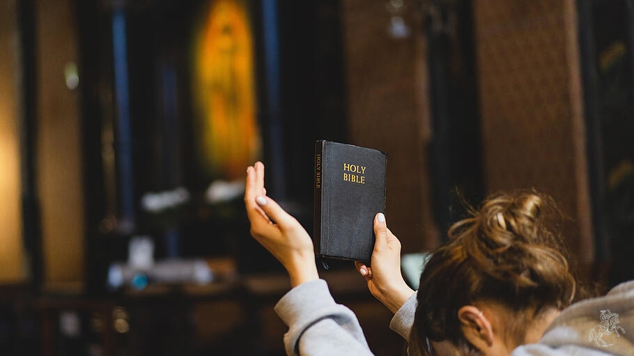 Frau hält in der rechten Hand die Bibel hoch zum Beten