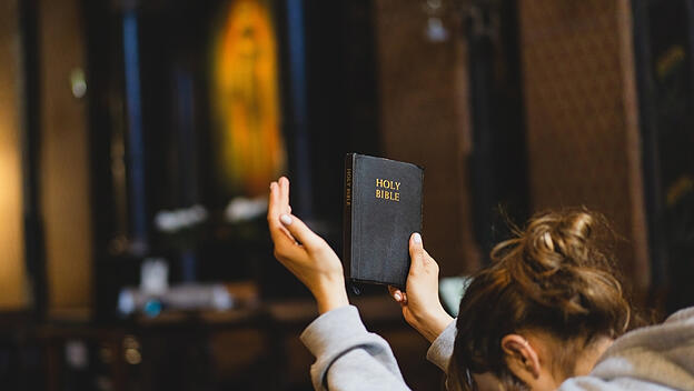 Frau hält in der rechten Hand die Bibel hoch zum Beten