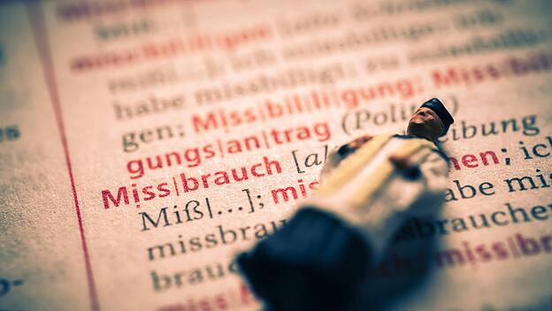 Miniaturfigur eines Priesters in einem Wörterbuch mit dem Wort Missbrauch