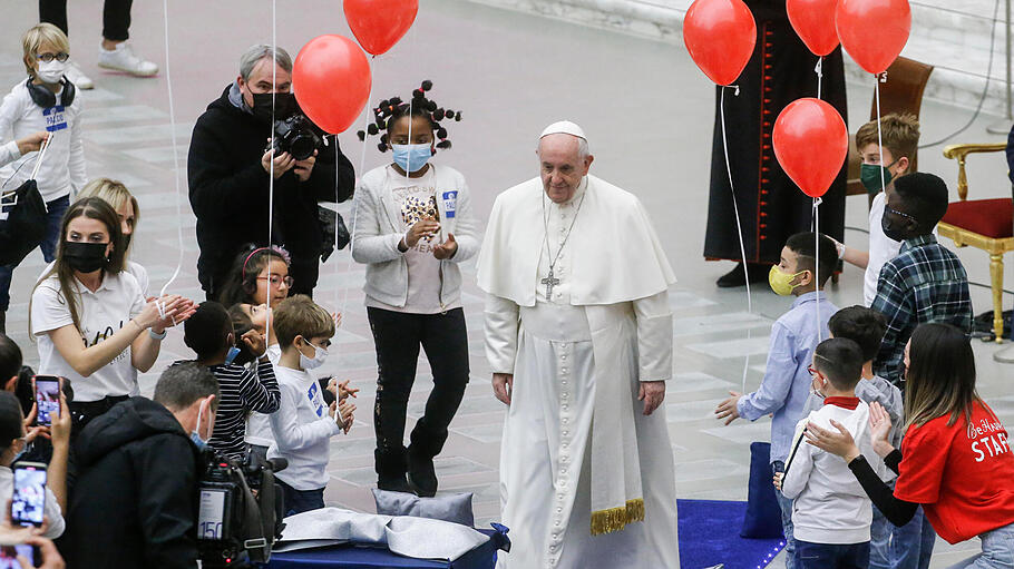 Papst Franziskus steht zwischen Luftballon haltenden Kindern