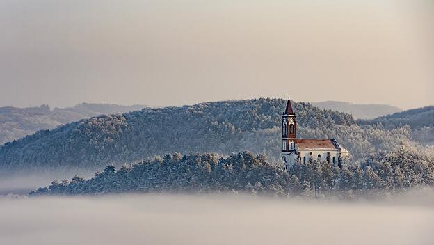 Eine Kirche auf einem Hügel ist von einem Meer aus Nebel umgeben