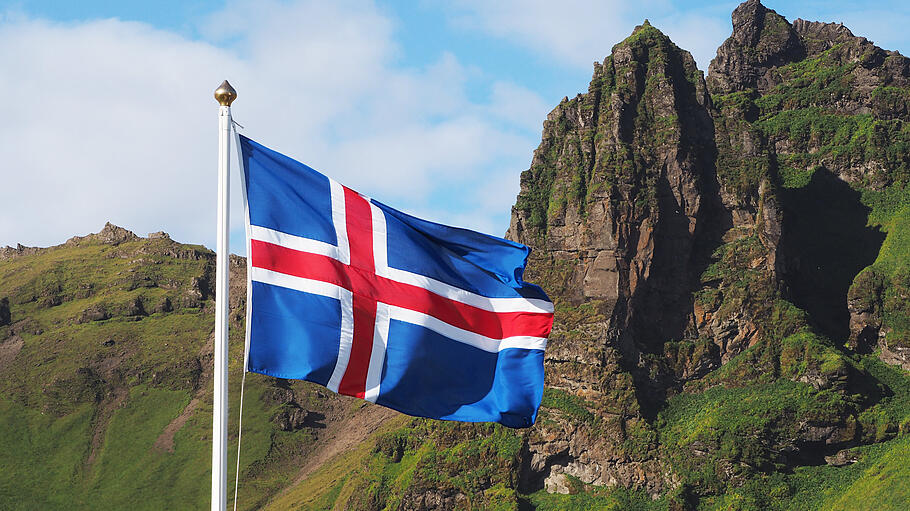 Flag of Iceland against the background of green mountains and blue sky