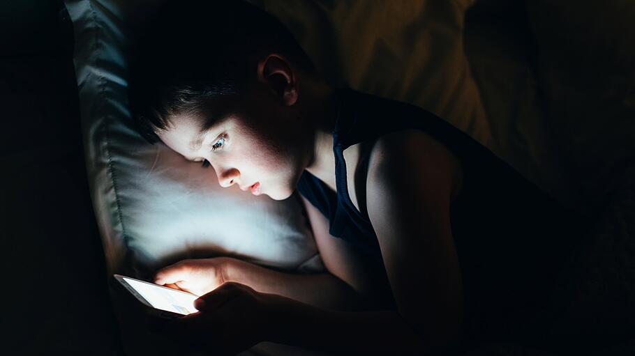 Ein sieben Jahre alter Junge mit Smartphone in der Nacht