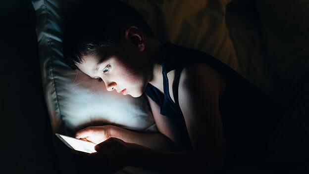 Ein sieben Jahre alter Junge mit Smartphone in der Nacht