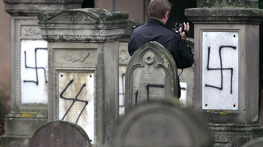 A French gendarme films tombstones desecrated by vandals with Nazi swastikas and anti-semitic slogan..