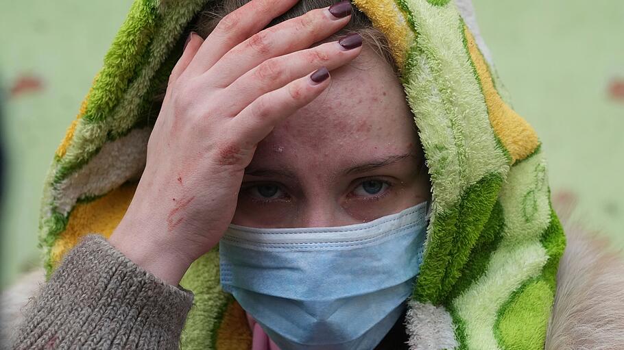 Verletzte Frau fasst sich vor einer durch einen Angriff in Mariupol an den Kopf