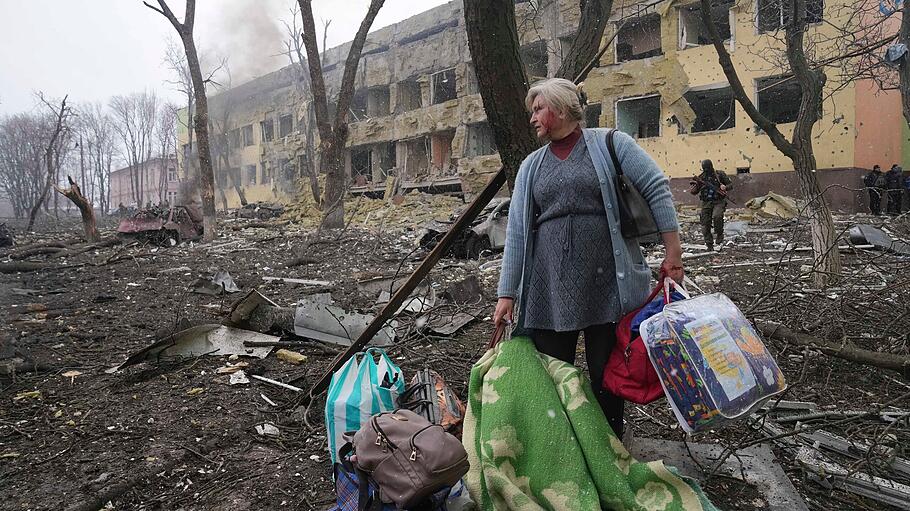 Ukraine-Krieg: Frau steht mit ihrem Gepäck vor beschädigten Geburtsklinik in Mariupol