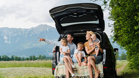 Family enjoying a road trip sitting on the open trunk of a car in nature