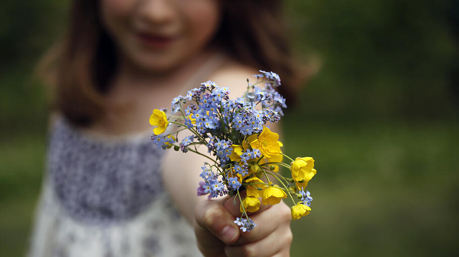 Mädchen mit selbst gepflückten Blumenstrauss aus bunten Blumen als Geschenk