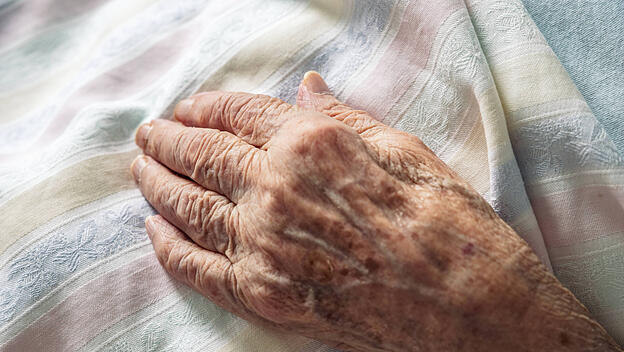 Winkled hand of an 100 old senior elderly women resting peacefully on hospital bedding. Concept of life, aging, health,