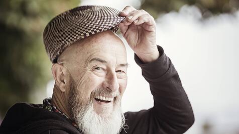 Ein fr&ouml;hlicher alter Mann mit Schirmm&uuml;tze im Gr&uuml;nen.