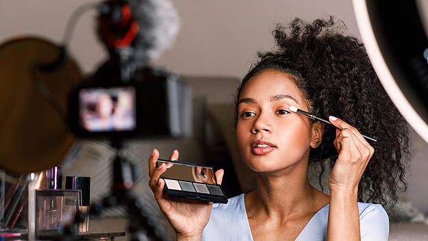 Female video blogger applying make up on face in living room