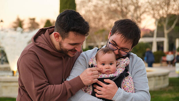 Homosexual happy couple playing with their baby in a baby carrier. Madrid, Community of Madrid, Spain CR_CRVI240216-1352