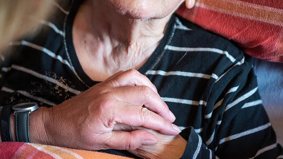 Die Leiterin eines ambulanten Dienstes drückt einer an Demenz und Parkinson erkrankten Patientin die Hand.