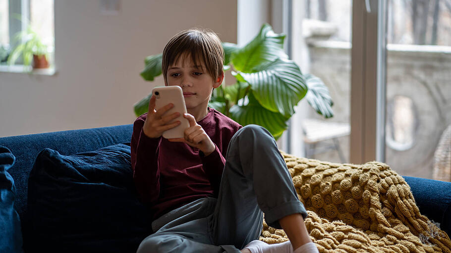 Entspannter kleiner Junge, der sein Smartphone benutzt