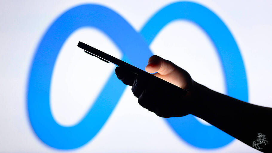 Smartphone in der Hand eines Nutzers, im Hintergrund das Markenlogo von Meta
