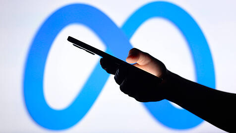 Smartphone in der Hand eines Nutzers, im Hintergrund das Markenlogo von Meta